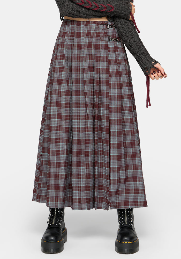 A model wearing a long, pleated plaid skirt in gray, burgundy, and white, styled with a dark gray knit sweater and black combat boots against a light gray studio background.