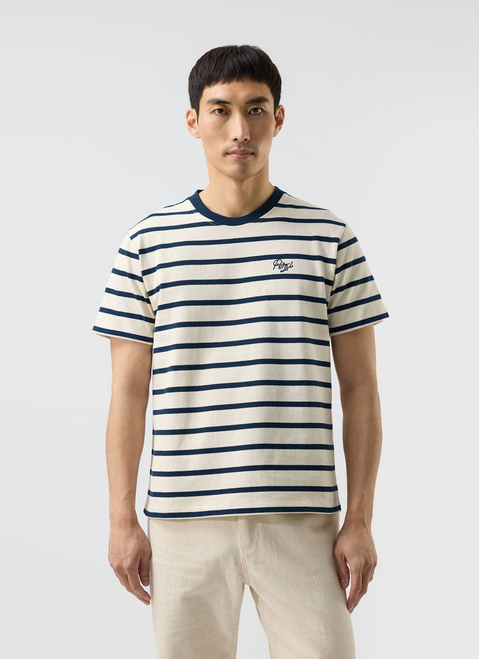 A man models the Percival Breton Stripe T-shirt in ecru and navy against a plain white studio background.