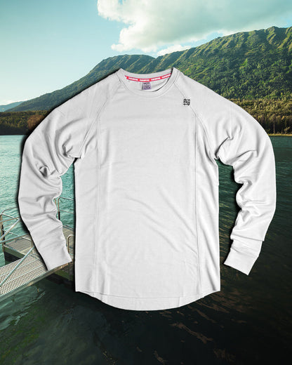 White long-sleeve shirt with brand logos on a dock with mountains and water in the background