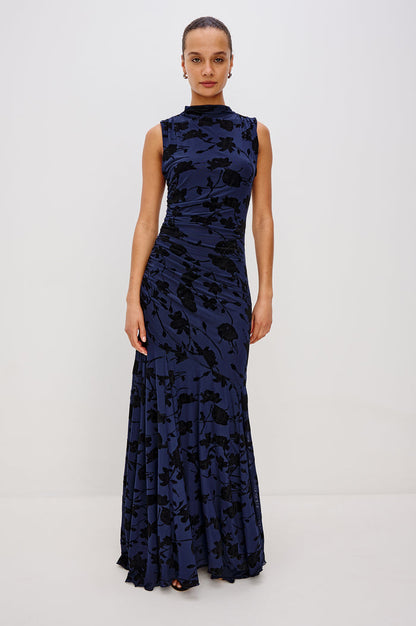 Cosmos Maxi-Length Dress with a Cowl Neck, Sleeveless, Form Fitting with a Ruched Side Seam Detail and an A-line Hem in Navy Tossed Roses Colorway. Full Body Front View Shown on Model.