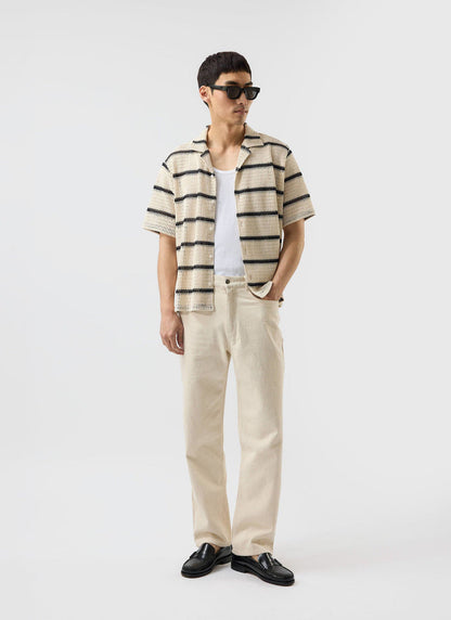 A model wears the Percival Crochet Groundsman Cuban Shirt in ecru with black stripes, styled open over a white vest.