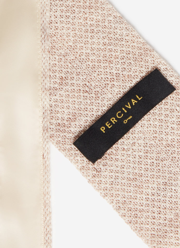A close-up of the textured oat marl linen and black brand label on the back of the Percival Linen Tie.