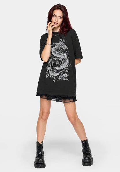 A model with dark red hair wearing an oversized black t-shirt dress featuring a large white dragon graphic on the front, styled with black lace-up combat boots against a light gray background.