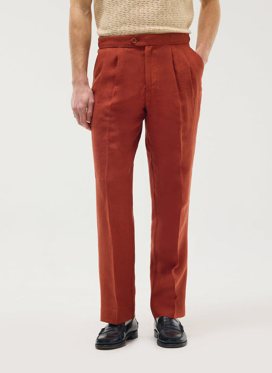 A model wears Percival's rust linen pleated tailored trousers with a cream knit top and black loafers.