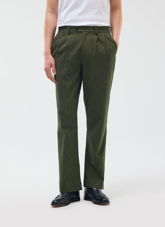 A model wears the Percival Pleated Tailored Trouser in forest green micro check, styled with a white tee and black loafers.