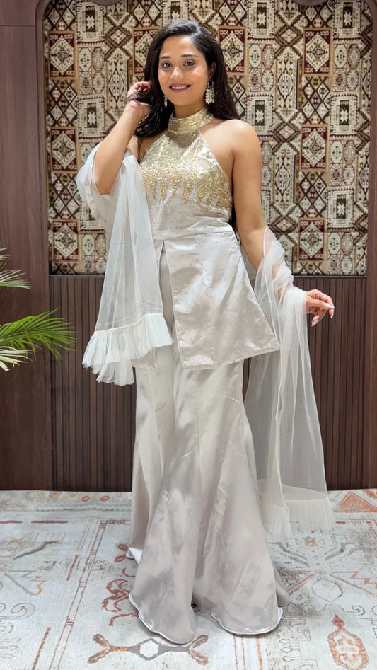 Woman in a white and gold traditional outfit with a patterned wall in the background