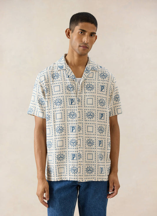 Cream linen-blend Percival Solis Heaton Cuban shirt with blue embroidered sun and 'P' motifs, shown on a model.