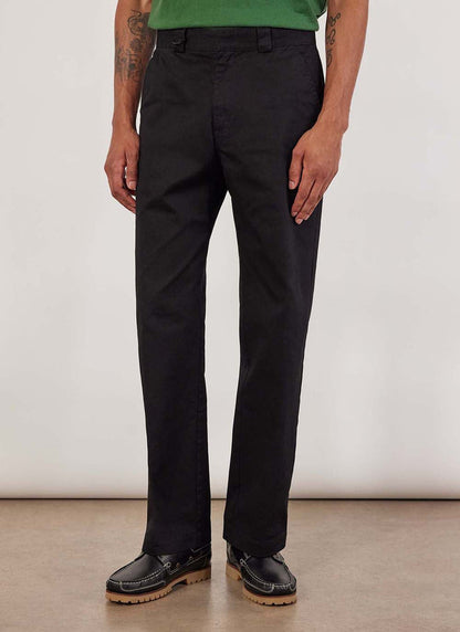 A model wears the Percival Stay Press Trousers in black cotton twill, paired with a green t-shirt and black shoes.