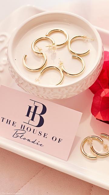 Gold rings in a white dish with 'The House of Blondie' card on a pink surface